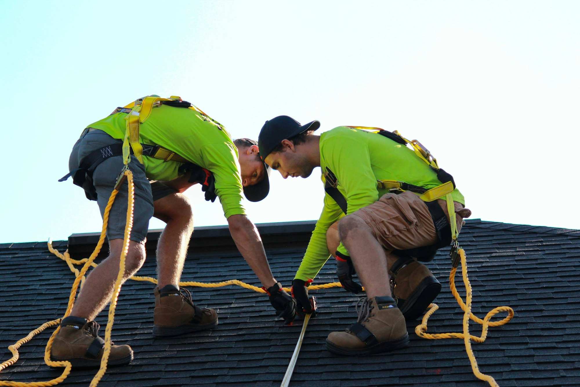 Two Kestrel roofers in safety harnesses fastening shingles
