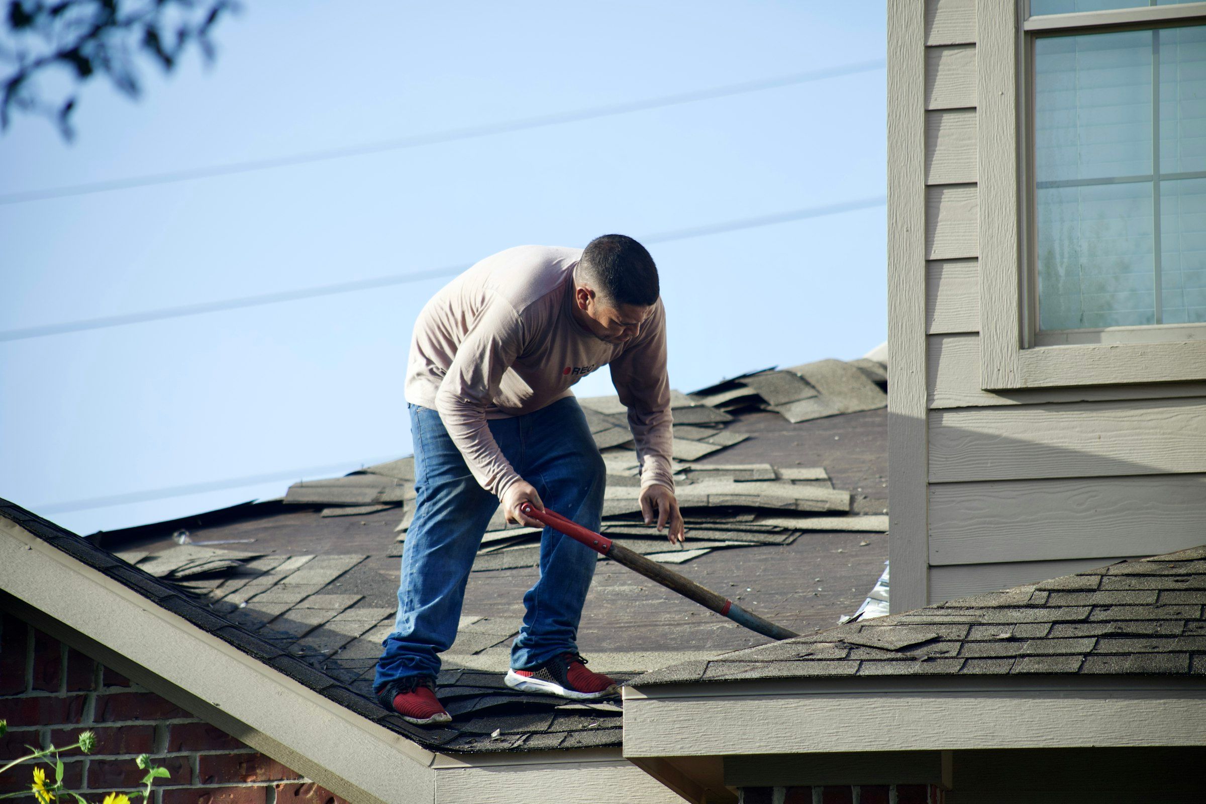 Roofer tearing off old shingles with a shovel