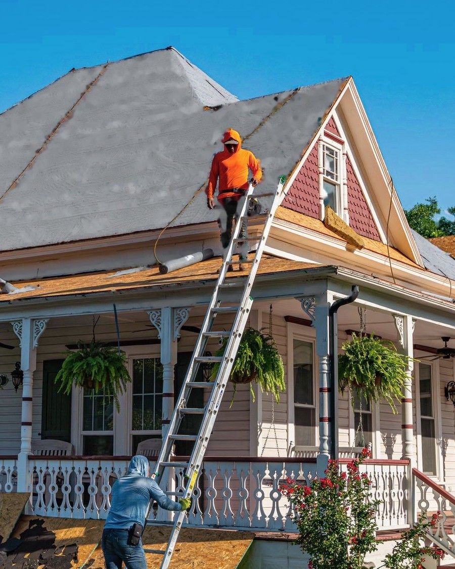Roofer on a ladder at the eave of a roof covered in new grey synthetic underlayment