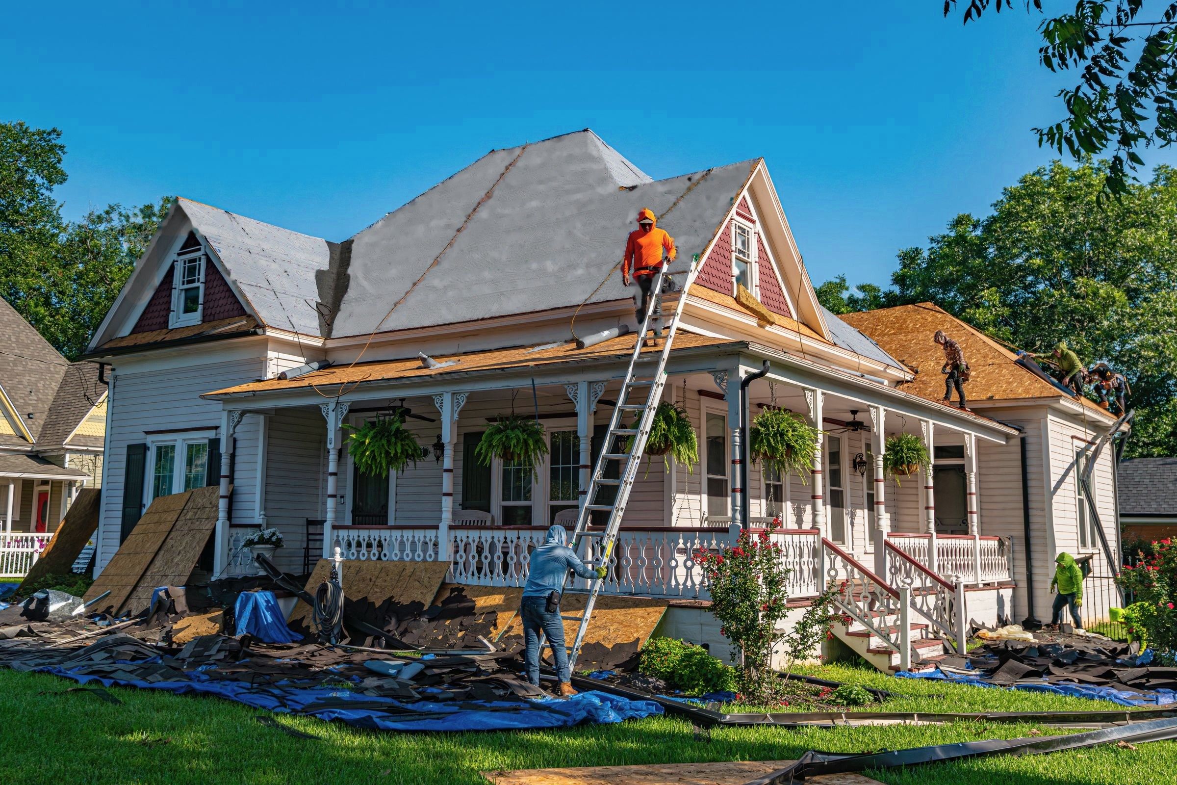 Crew replacing the roof of a white two-story house with a wraparound porch