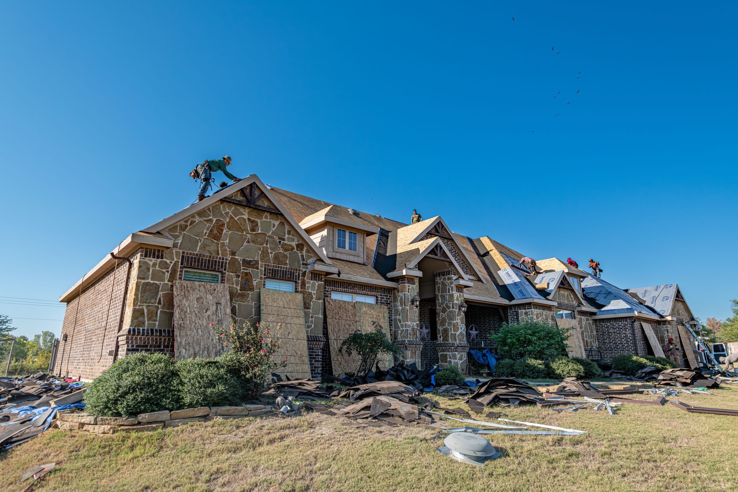 Stone-front home mid-replacement with crew on the roof